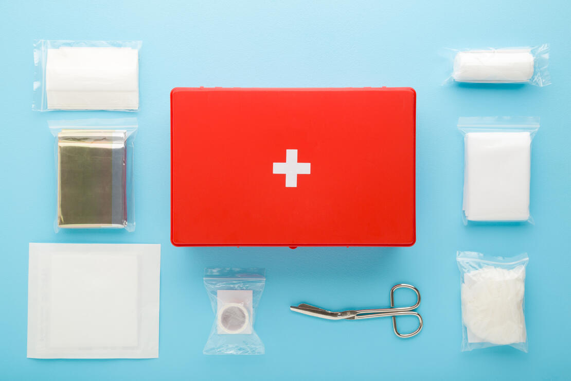 Different medical accessories in packages around red first aid kit box on light blue table background.