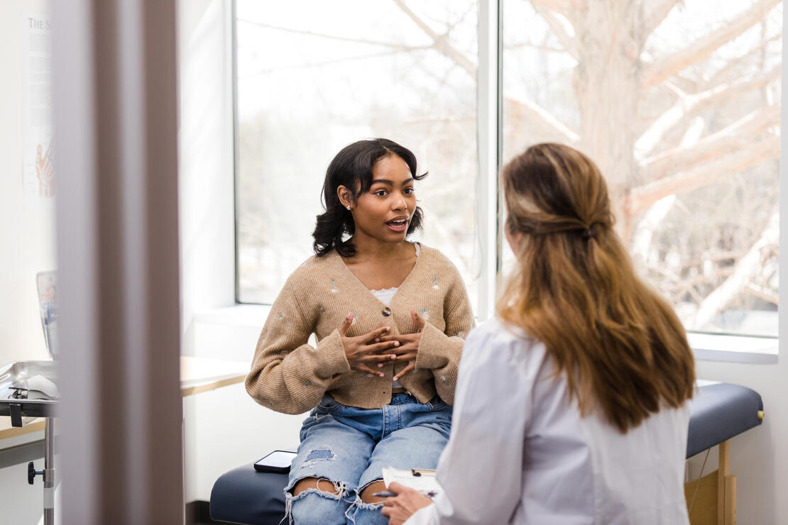 Teen girl sitting on cot and gesturing while discussing her health with her doctor