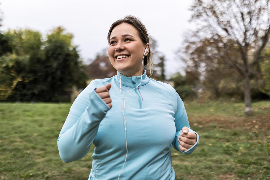 Midsize woman smiling as she runs with headphones in