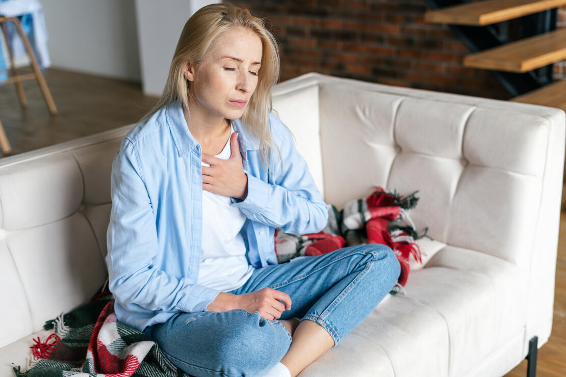 Exhausted, worried woman feeling pain ache, touching her chest, having heart attack or disease symptom, suffers from heartache sitting at home alone