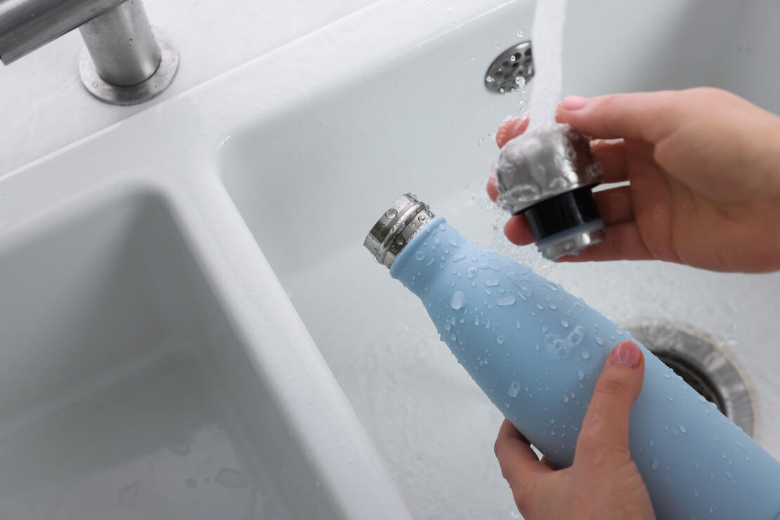 Woman washing thermos bottle in kitchen, above view