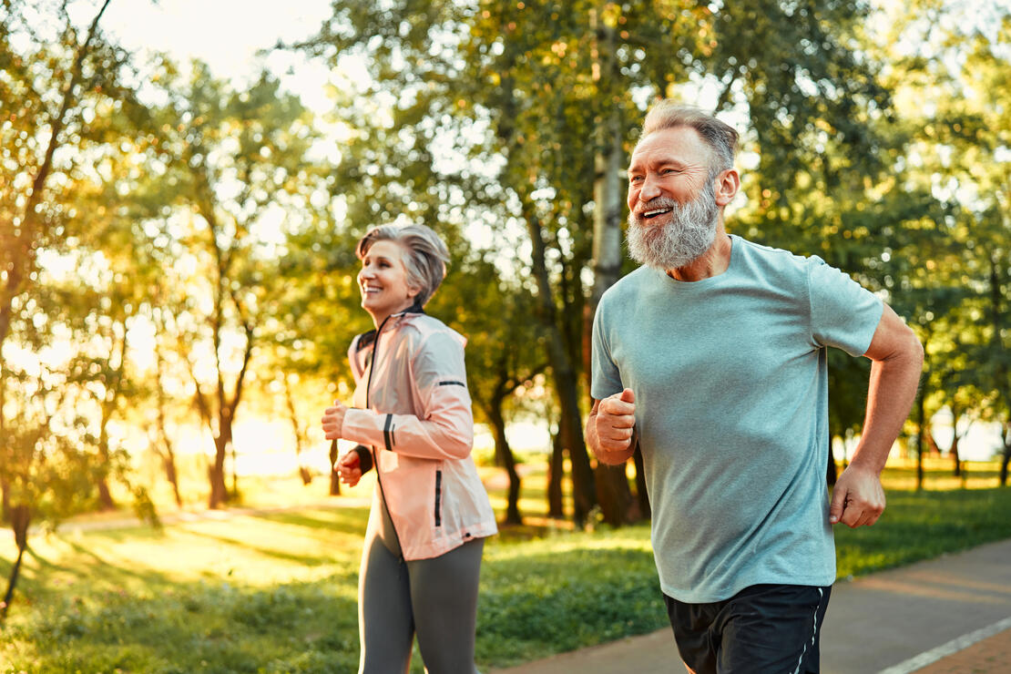 Mature fitness people feeling contentment when running together in park. Cheerful loving spouses standing for healthy lifestyle and training every day outdoors.