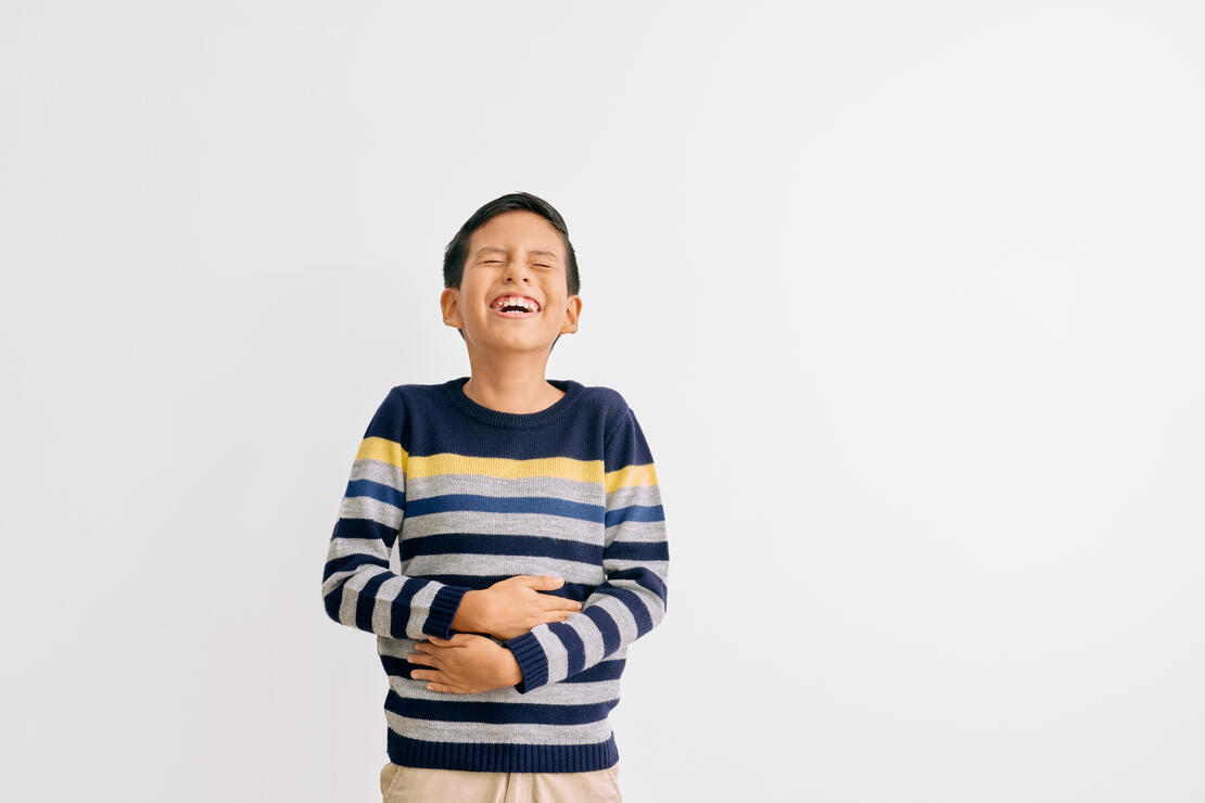 Young boy laughing and holding stomach in front of a white backdrop.
