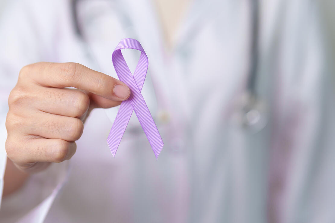 Clinician in a white coat holding a purple ribbon for Domestic Violence Awareness Month