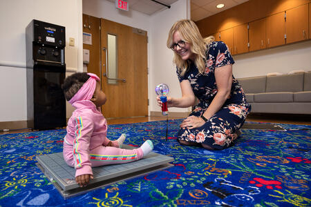 Researcher smiling down at an infant sitting on a force plate