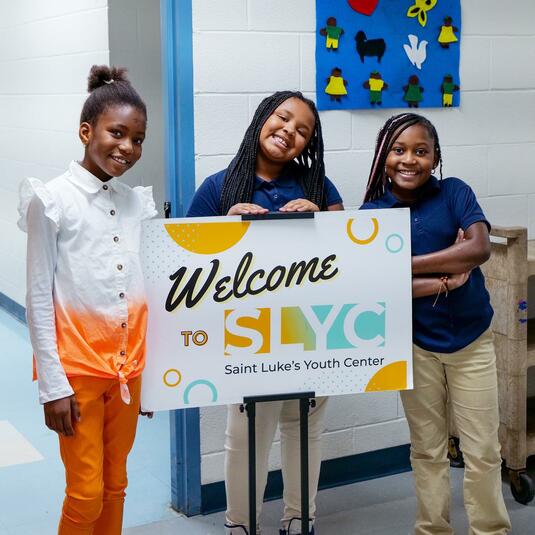 Three children holding up a SLYC sign