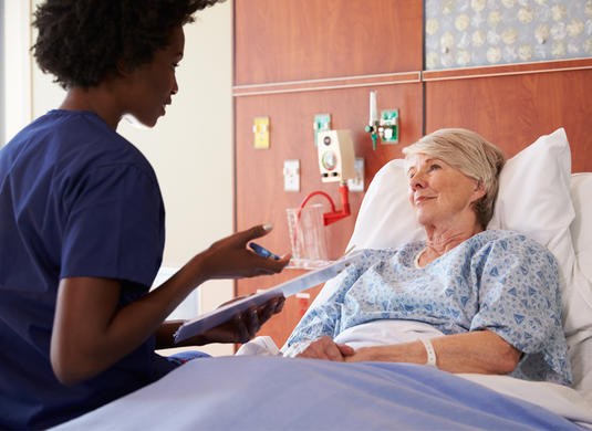 A nurse talking with a patient in a hospital bed. A nurse talking with a patient in a hospital bed.